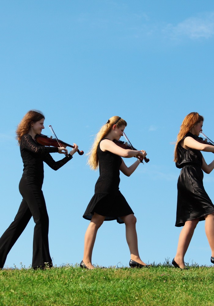 Four musicians go and playing violins against sky